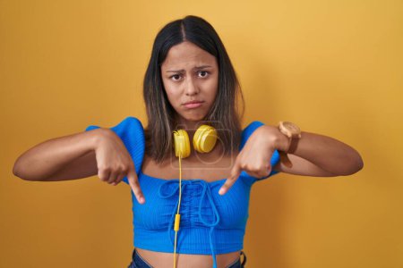 Photo for Hispanic young woman standing over yellow background pointing down looking sad and upset, indicating direction with fingers, unhappy and depressed. - Royalty Free Image