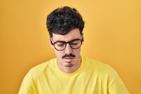 Téléchargez les photos : Homme hispanique portant des lunettes debout sur fond jaune avec la main sur le ventre parce que l'indigestion, la maladie douloureuse se sent mal. concept de douleur. - en image libre de droit