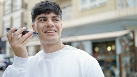 Téléchargez les photos : Jeune homme hispanique envoyant un message vocal avec smartphone sur la terrasse du café - en image libre de droit