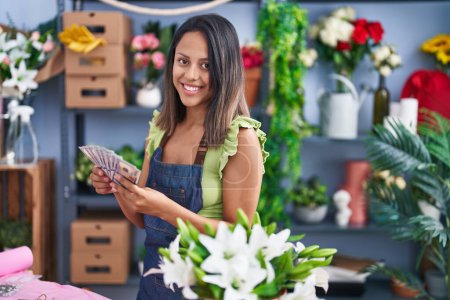 Photo for Young hispanic woman florist smiling confident holding dollars at florist store - Royalty Free Image