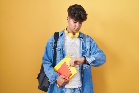 Foto de Adolescente hispano con mochila estudiantil y libros revisando la hora en el reloj de pulsera, relajado y confiado - Imagen libre de derechos