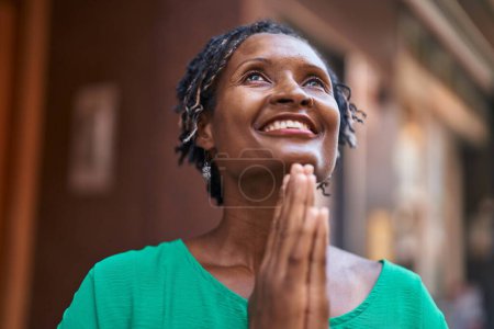 Foto de Mujer afroamericana de mediana edad sonriendo confiada rezando en la calle - Imagen libre de derechos