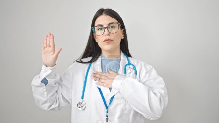 Téléchargez les photos : Jeune femme hispanique médecin faire un serment avec la main sur la poitrine sur fond blanc isolé - en image libre de droit