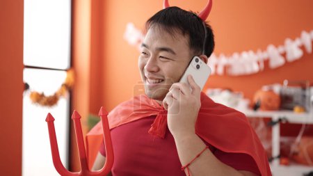 Téléchargez les photos : Jeune homme chinois portant costume diable parler sur smartphone à la maison - en image libre de droit
