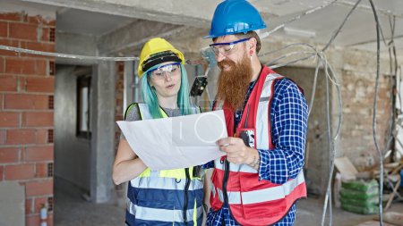 Téléchargez les photos : Constructeurs hommes et femmes lisant le projet de maison parlant sur le chantier de construction - en image libre de droit