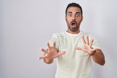 Photo for Hispanic man with beard standing over isolated background afraid and terrified with fear expression stop gesture with hands, shouting in shock. panic concept. - Royalty Free Image