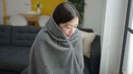 Photo for Young chinese woman covering with blanket for cold sitting on sofa at home - Royalty Free Image