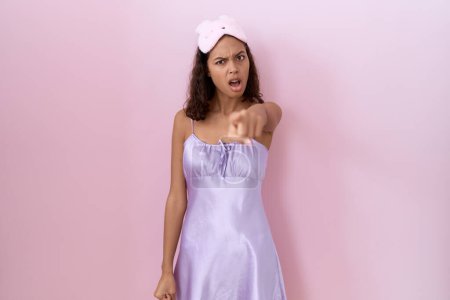 Photo for Young hispanic woman wearing sleep mask and nightgown pointing displeased and frustrated to the camera, angry and furious with you - Royalty Free Image