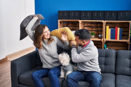 Foto de Hombre y mujer peleando con cojín sentado en sofá con perro en casa - Imagen libre de derechos
