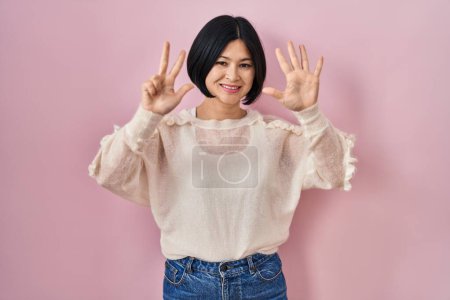 Photo for Young asian woman standing over pink background showing and pointing up with fingers number eight while smiling confident and happy. - Royalty Free Image