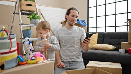 Téléchargez les photos : Père et fils déballer la boîte en carton en utilisant un smartphone à la nouvelle maison - en image libre de droit