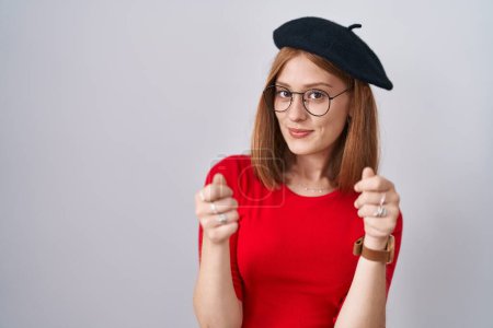 Photo for Young redhead woman standing wearing glasses and beret doing money gesture with hands, asking for salary payment, millionaire business - Royalty Free Image