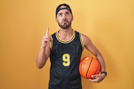 Photo for Middle age bald man holding basketball ball over yellow background pointing up looking sad and upset, indicating direction with fingers, unhappy and depressed. - Royalty Free Image