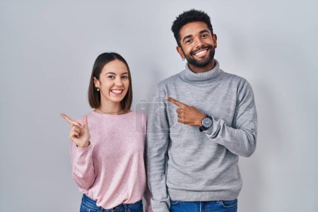 Photo for Young hispanic couple standing together cheerful with a smile on face pointing with hand and finger up to the side with happy and natural expression - Royalty Free Image