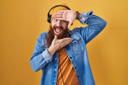 Téléchargez les photos : Homme caucasien à longue barbe écoutant de la musique à l'aide d'écouteurs souriant gai jouer jeter un coup d'oeil un boo avec les mains montrant le visage. surpris et sortis - en image libre de droit