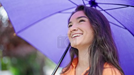 Foto de Joven hermosa mujer hispana sonriendo confiada sosteniendo paraguas en el parque - Imagen libre de derechos