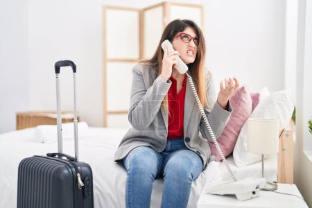 Foto de Mujer hispana joven trabajadora de negocios hablando por teléfono con recepción en la habitación del hotel - Imagen libre de derechos