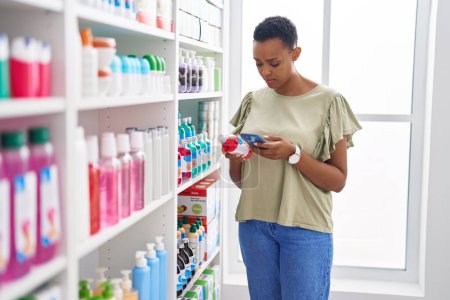 Téléchargez les photos : Femme afro-américaine cliente utilisant un smartphone tenant une bouteille de médicament à la pharmacie - en image libre de droit