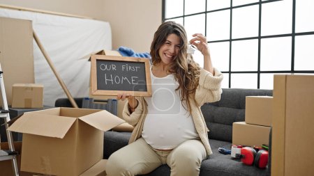 Photo for Young pregnant woman smiling confident holding new house keys and blackboard at new home - Royalty Free Image