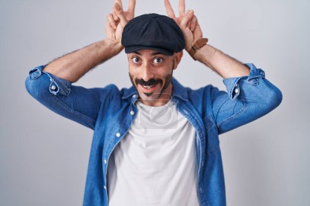Téléchargez les photos : Homme hispanique avec barbe debout sur fond isolé posant drôle et fou avec les doigts sur la tête comme des oreilles de lapin, souriant gai - en image libre de droit
