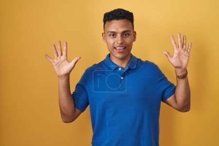 Téléchargez les photos : Young hispanic man standing over yellow background showing and pointing up with fingers number ten while smiling confident and happy. - en image libre de droit