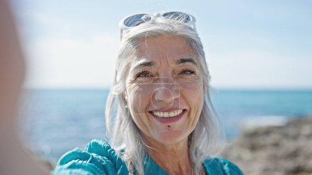 Photo for Middle age grey-haired woman tourist making selfie by the camera at beach - Royalty Free Image