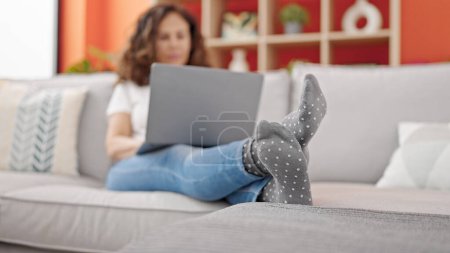 Foto de Mujer hispana de mediana edad usando portátil moviendo el pie en casa - Imagen libre de derechos