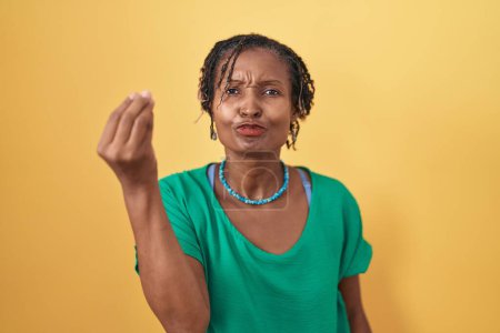 Foto de Mujer africana con rastas de pie sobre fondo amarillo haciendo gesto italiano con la mano y los dedos expresión de confianza - Imagen libre de derechos