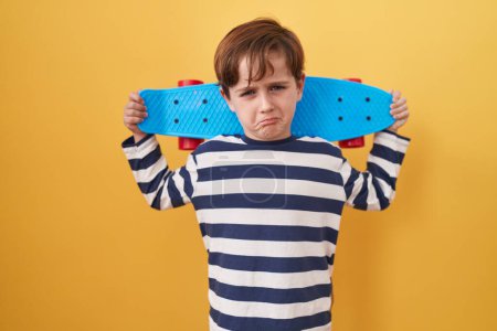 Téléchargez les photos : Petit garçon caucasien tenant le patin sur fond jaune déprimé et inquiet pour la détresse, pleurant en colère et effrayé. triste expression. - en image libre de droit
