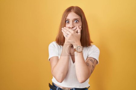 Photo for Young redhead woman standing over yellow background shocked covering mouth with hands for mistake. secret concept. - Royalty Free Image