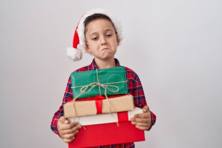Photo for Little hispanic boy wearing christmas hat holding presents depressed and worry for distress, crying angry and afraid. sad expression. - Royalty Free Image