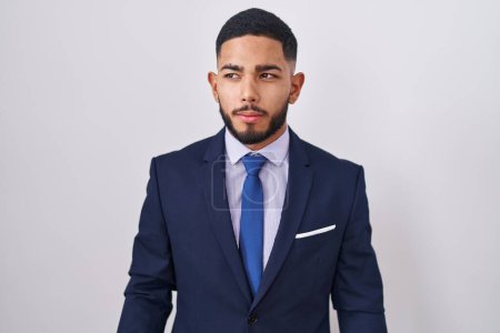 Téléchargez les photos : Jeune homme hispanique portant costume d'affaires et cravate souriant regardant vers le côté et regardant loin en pensant. - en image libre de droit