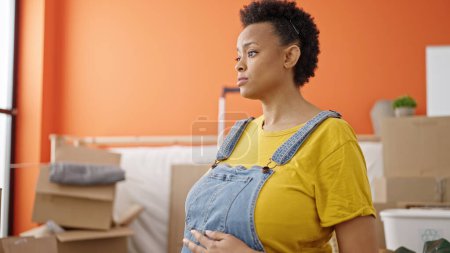 Foto de Mujer embarazada joven tocando el vientre con expresión relajada en un nuevo hogar - Imagen libre de derechos