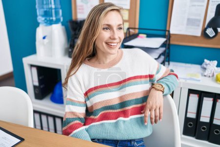 Téléchargez les photos : Jeune femme blonde travailleur d'affaires souriant confiant assis sur la table au bureau - en image libre de droit