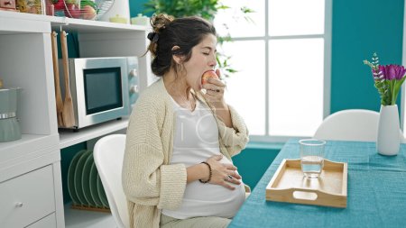 Téléchargez les photos : Jeune femme enceinte prenant le petit déjeuner toucher le ventre à la salle à manger - en image libre de droit