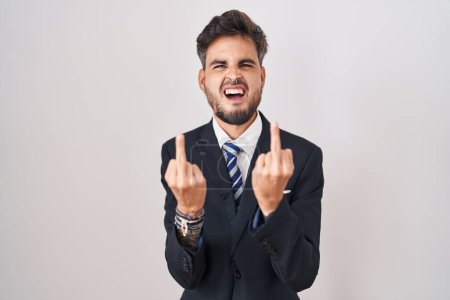 Foto de Young hispanic man with tattoos wearing business suit and tie showing middle finger doing fuck you bad expression, provocation and rude attitude. screaming excited - Imagen libre de derechos