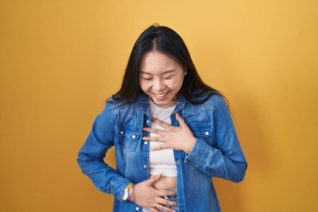 Photo for Young asian woman standing over yellow background smiling and laughing hard out loud because funny crazy joke with hands on body. - Royalty Free Image