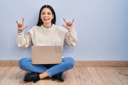 Photo for Young woman using laptop sitting on the floor at home shouting with crazy expression doing rock symbol with hands up. music star. heavy music concept. - Royalty Free Image