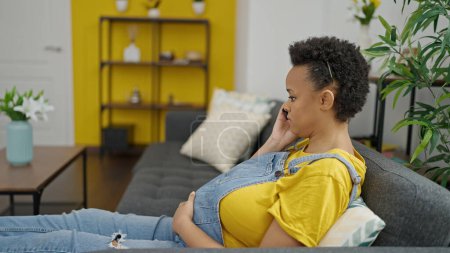 Foto de Mujer embarazada joven hablando en smartphone con expresión seria en casa - Imagen libre de derechos