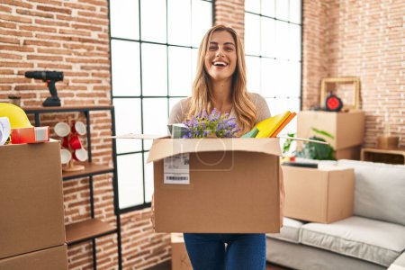 Photo for Young blonde woman moving to a new home holding cardboard box smiling and laughing hard out loud because funny crazy joke. - Royalty Free Image