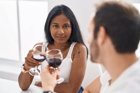 Foto de Hombre y mujer interracial pareja bebiendo vino sentado en la mesa en casa - Imagen libre de derechos
