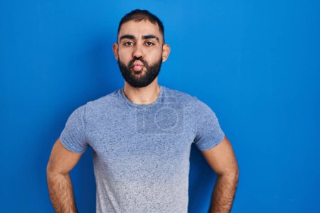 Photo for Middle east man with beard standing over blue background making fish face with lips, crazy and comical gesture. funny expression. - Royalty Free Image
