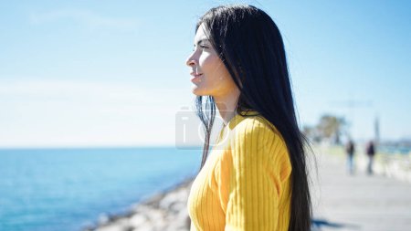 Téléchargez les photos : Jeune belle femme hispanique regardant vers le côté avec une expression détendue au bord de la mer - en image libre de droit