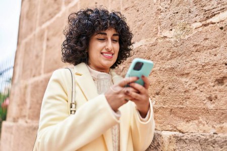 Foto de Joven mujer de Oriente Medio excusa sonriendo confiado usando teléfono inteligente en la calle - Imagen libre de derechos
