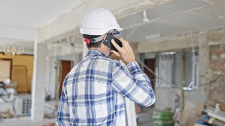 Foto de Constructor hombre de mediana edad hablando en el teléfono inteligente en el sitio de construcción - Imagen libre de derechos
