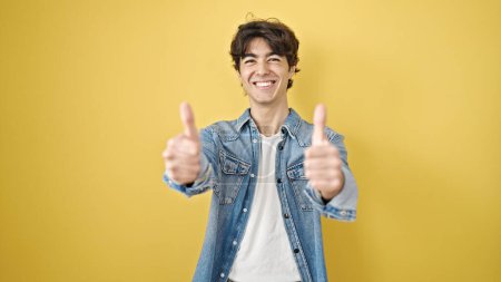 Photo for Young hispanic man smiling with thumbs up over isolated yellow background - Royalty Free Image