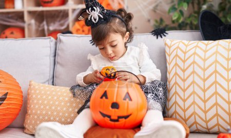 Foto de Adorable chica hispana con disfraz de halloween sosteniendo caramelos de canasta de calabaza en casa - Imagen libre de derechos