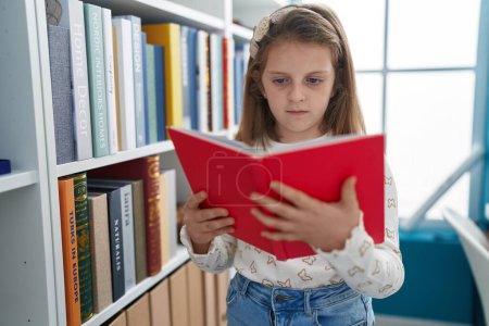 Foto de Adorable chica rubia estudiante lectura libro en el aula - Imagen libre de derechos