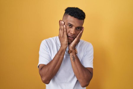 Photo for Young hispanic man standing over yellow background tired hands covering face, depression and sadness, upset and irritated for problem - Royalty Free Image