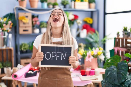Photo for Young blonde woman working at florist holding open sign angry and mad screaming frustrated and furious, shouting with anger looking up. - Royalty Free Image